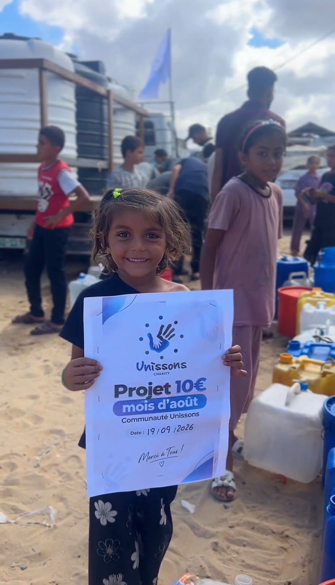Une petite fille de Gaza tient l'affiche « Projet 10 € » d'Unissons Charity lors d'une distribution d'eau potable
